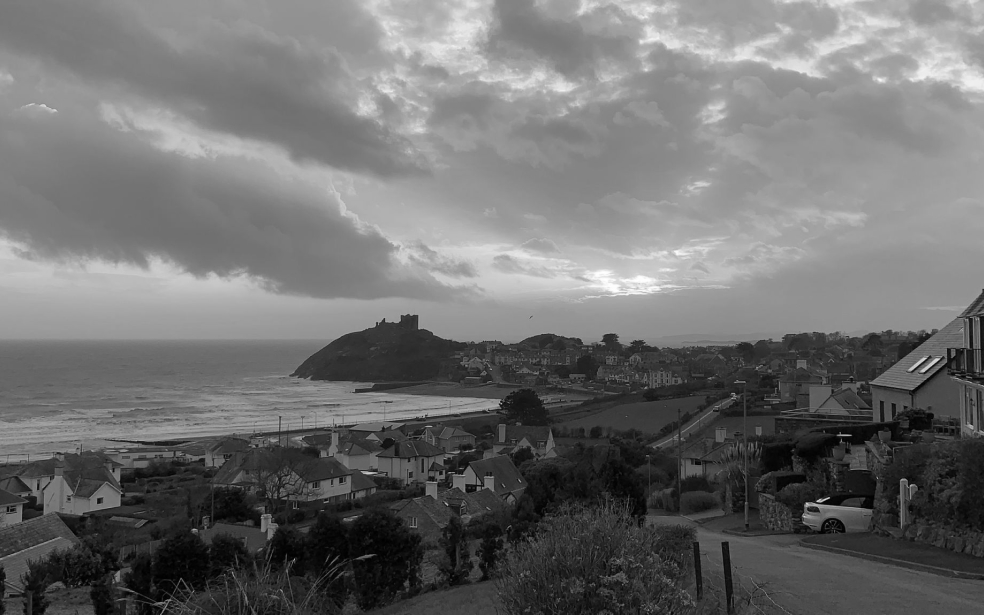 Vista en blanco y negro de una ciudad costera con un castillo en una colina junto al mar.